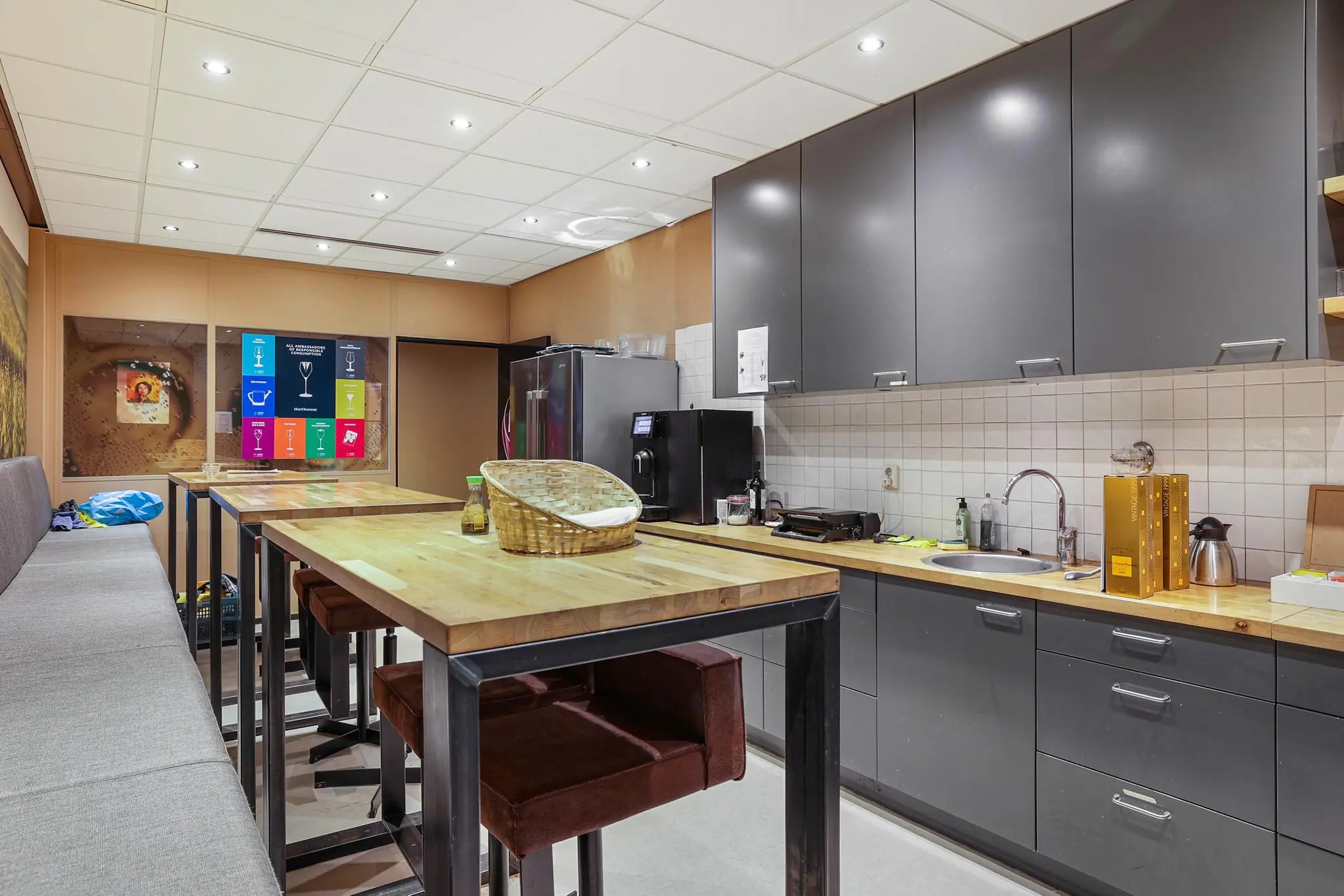 Moderne kantoorkeuken met houten tafels, grijze kasten en een koffiehoek aan de Oude Utrechtseweg.